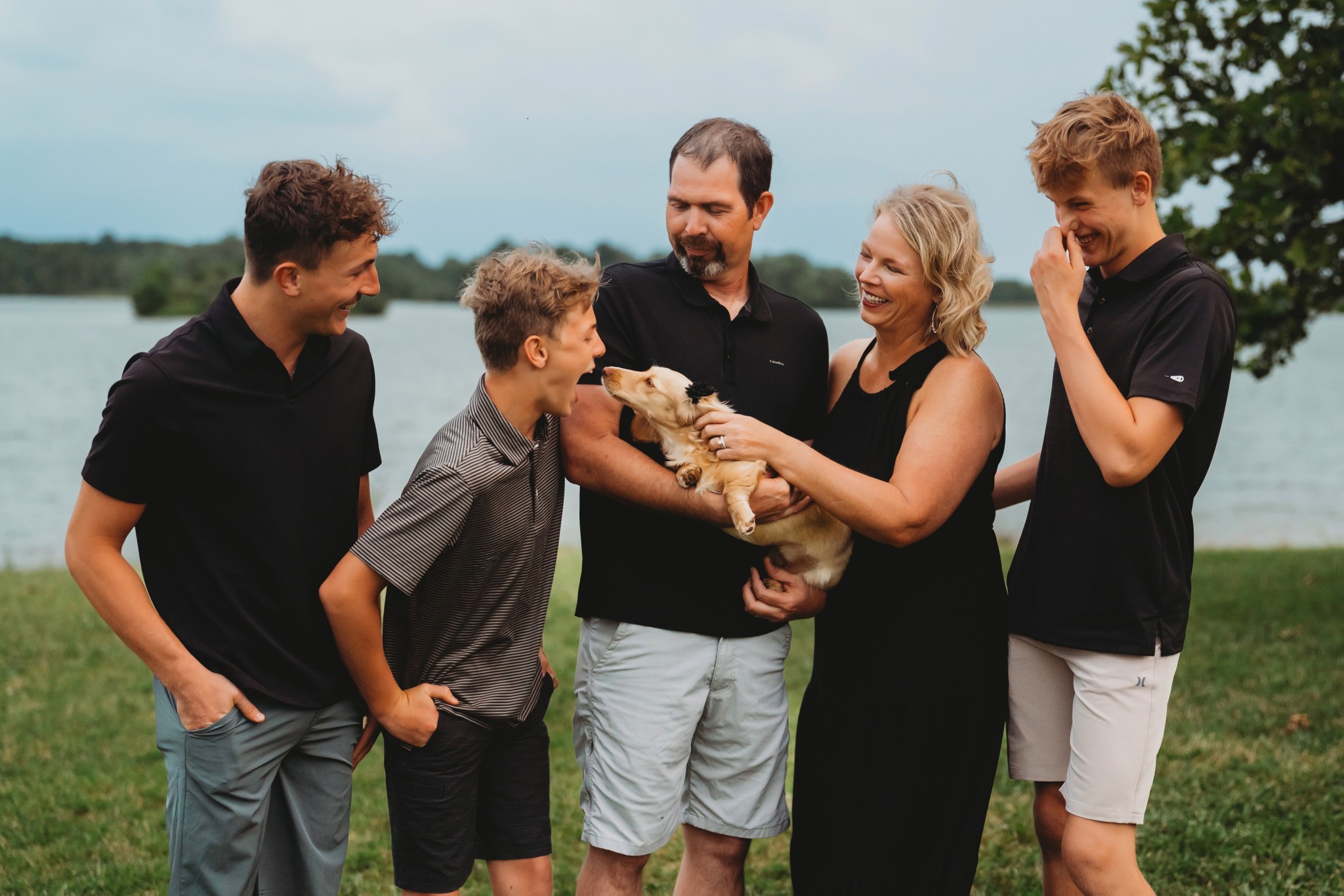 The Golliher family laughing together by the lake with their dog